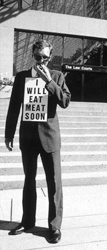 Black and white photo of Gibson eating the meat hors d'oeuvre on the steps of the Vancouver Law Courts