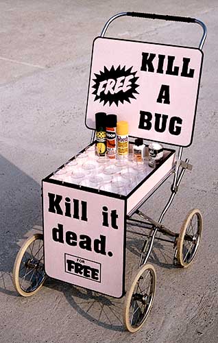 Color photo of a converted baby buggy with two signs reading "Free Kill a Bug" and "Kill it dead for free" with a box of insects in the middle