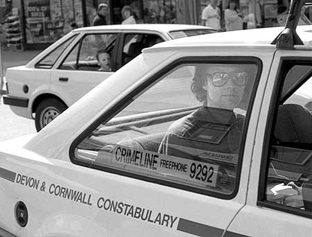 Black and white photo of Gibson sitting in the back of the police car being driven to the police station
