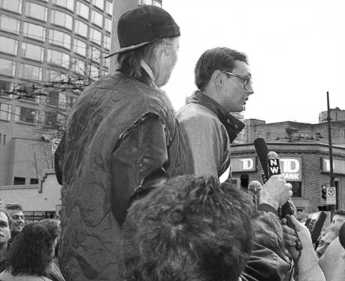 Black and white photo of Susi and Gibson standing on a street planter overlooking the crowd