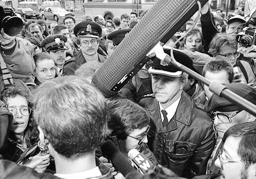 Black and white photo of Gibson encountering a large crowd of police, journalists and protesters